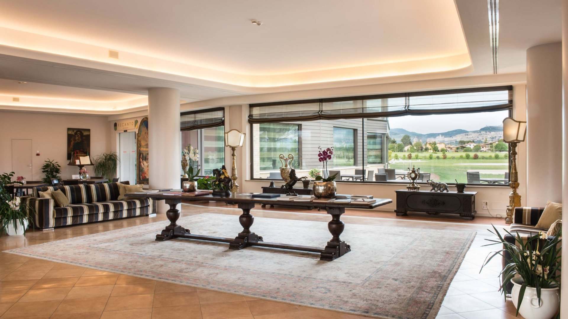 Hotel a 10 minuti di macchina da Assisi e la Basilica di San Francesco e il suo centro storico, 3 minuti di macchina dalla Porziuncola Sala con ampio tavolo, divani a righe e grandi finestre con vista sul paesaggio