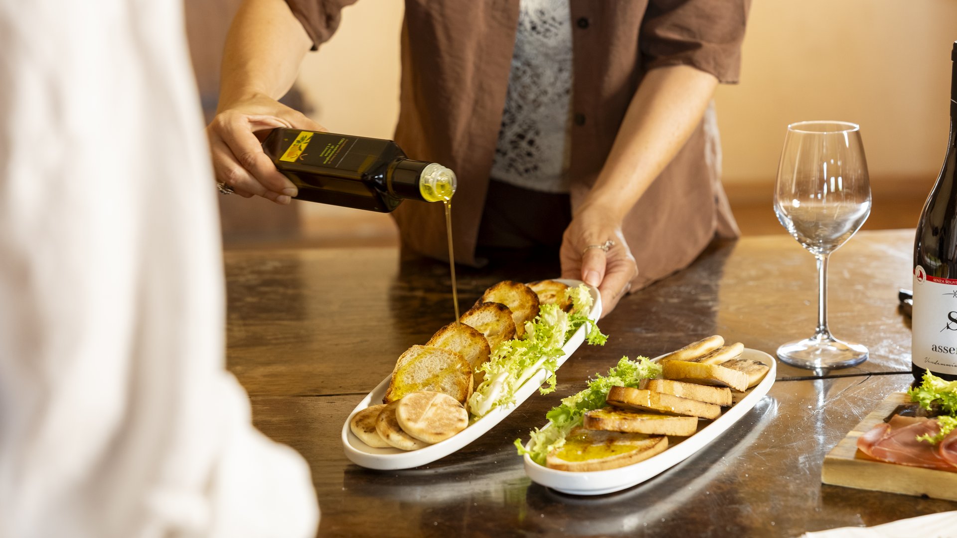 Un hotel vicino ad Assisi con mezza pensione da sogno Persona versa olio d'oliva su fette di pane tostato con insalata su piatti bianchi