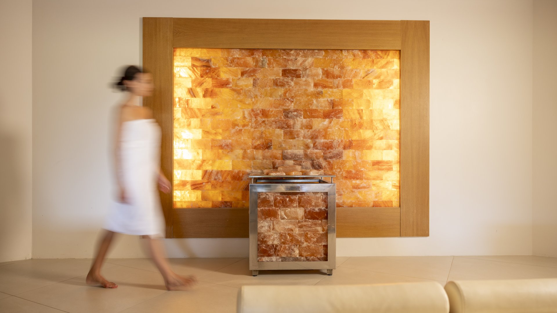 Assisi Cantico SPA - La tua SPA ad Assisi, Perugia, nell' Umbria più bella! Percorsi Benessere Massaggi Idee Regalo per Adulti e Bambini Donna in accappatoio bianco che cammina davanti a una parete illuminata di sale rosa